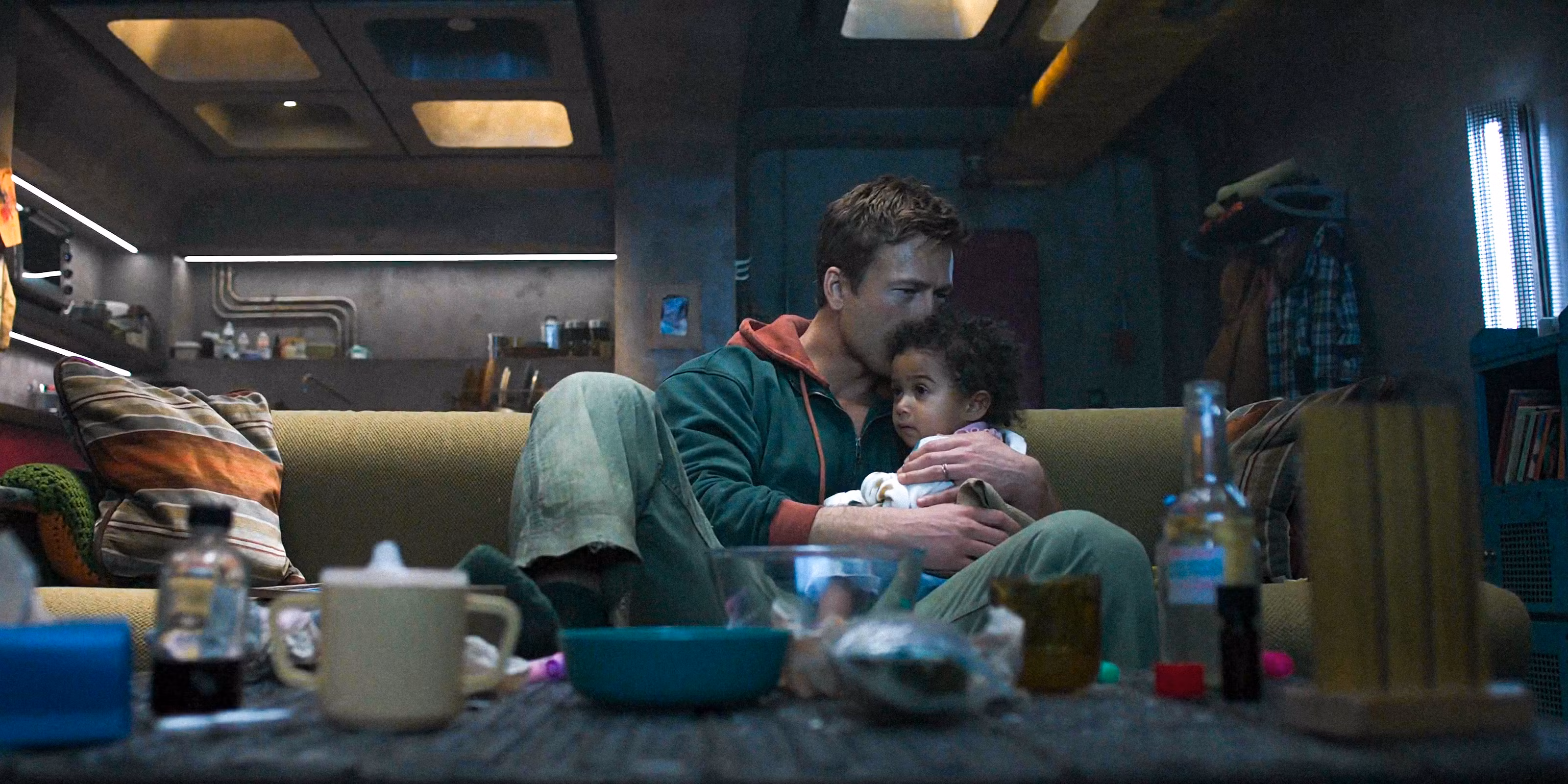 A white man kisses the head of his Black infant daughter while sitting on a couch.